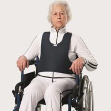 Una mujer en silla de ruedas está sentada sobre un fondo blanco y lleva un chaleco de respaldo para silla de ruedas.