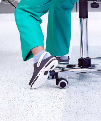 Une femme portant des sabots WOCK est assise sur une chaise dans un cabinet médical.