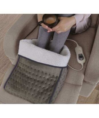 Una mujer sentada en una silla con una taza de café y un calientapiés eléctrico.