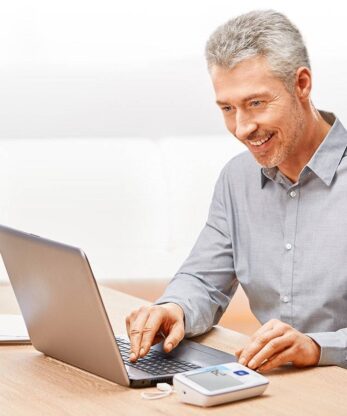 Un hombre sentado en una mesa con un tensiómetro Veroval Duo Control.