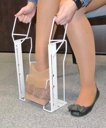 Une femme utilise un porte-chaussettes pour enfiler ses chaussettes en se tenant les pieds sur une chaise.