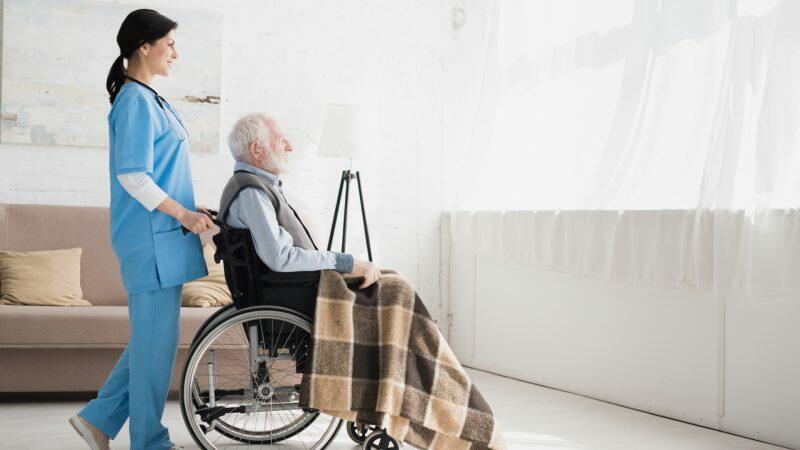 A nurse is helping an elderly man in a wheelchair.