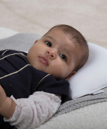 A baby lying on a blanket with a BUMI Baby Pillow.