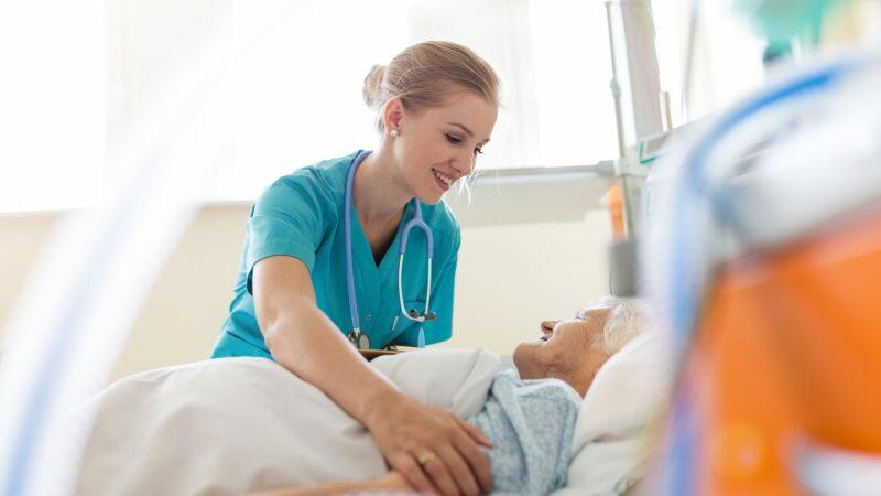 A nurse is touching an elderly woman in a hospital bed.