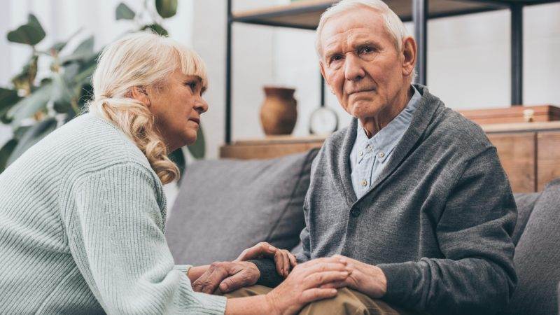 An elderly man and a woman talking on a sofa.