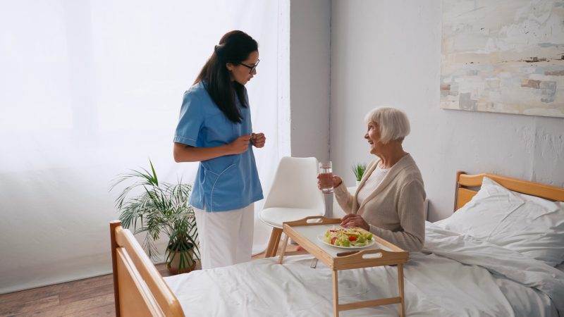 A nurse is talking to an elderly woman in bed.