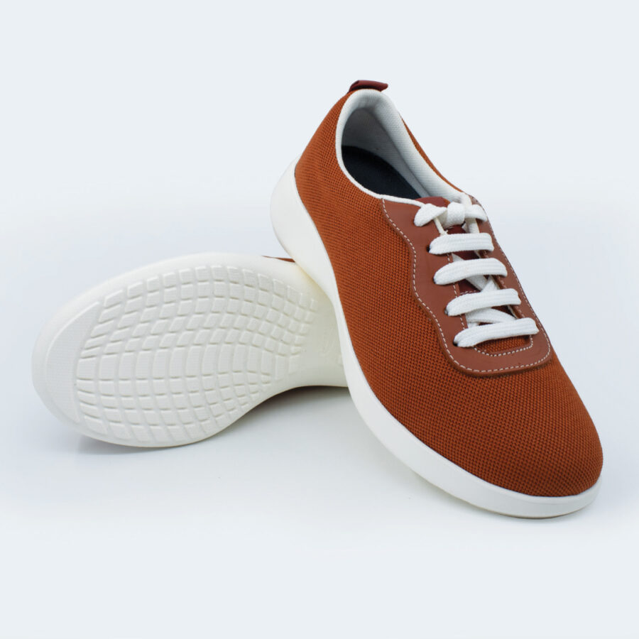 A pair of brown Wash'Go Sport knitted sneakers with white soles and white laces, shown against a light background. One shoe stands upright while the other lies on its side, showing off its textured sole.