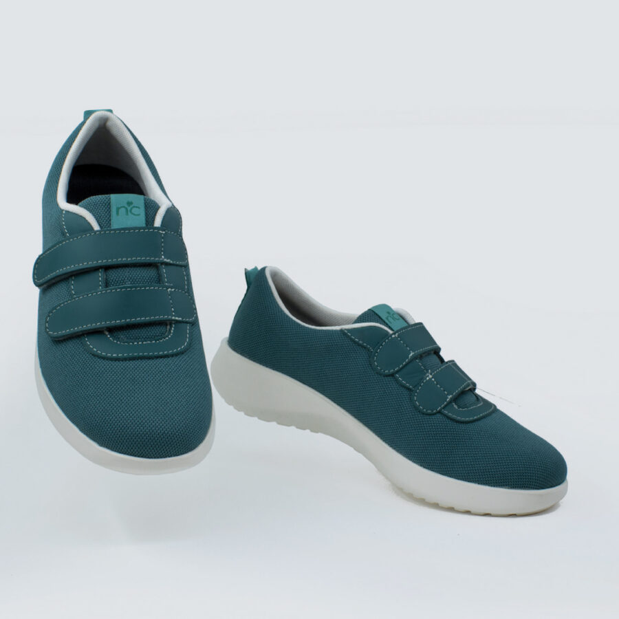 Une paire de chaussures de sport bleu jade avec des fermetures velcro sur un fond blanc.