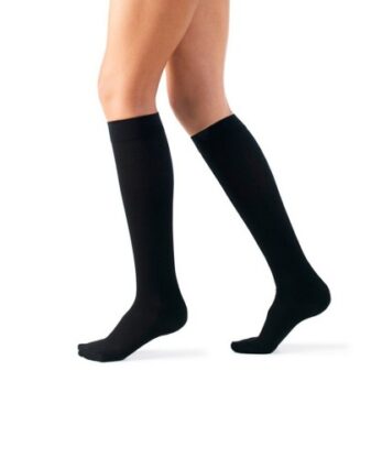 Una persona lleva calcetines de algodón AD 140 DEN a la altura de la rodilla, de pie sobre una pierna, sobre un fondo blanco liso.