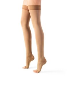 A person wearing Lycra AG Class II thigh-high compression stockings from Meias Terapêuticas in beige, standing against a white background.